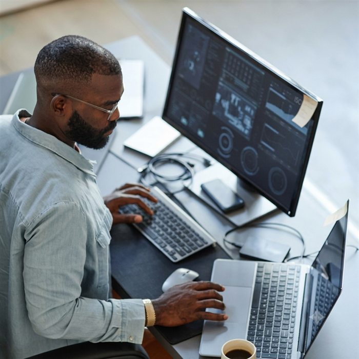Developer working across a monitor and laptop with coffee in hand